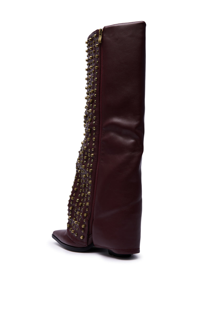 The AZALEA WANG AGUSTUE BURGUNDY STUDDED WESTERN BOOT is a tall, dark burgundy faux leather western boot with a flat heel, gold studs on the front panel, an outside gold zipper, and shown against a white background.