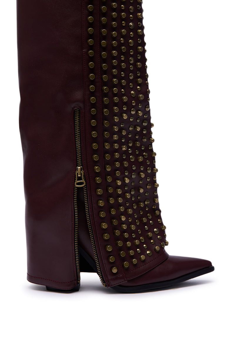 A close-up of the AZALEA WANG AGUSTUE Burgundy Studded Western Boot in faux leather, showcasing gold front studs, a partially unzipped gold side zipper, pointed toe, and wedge heel.