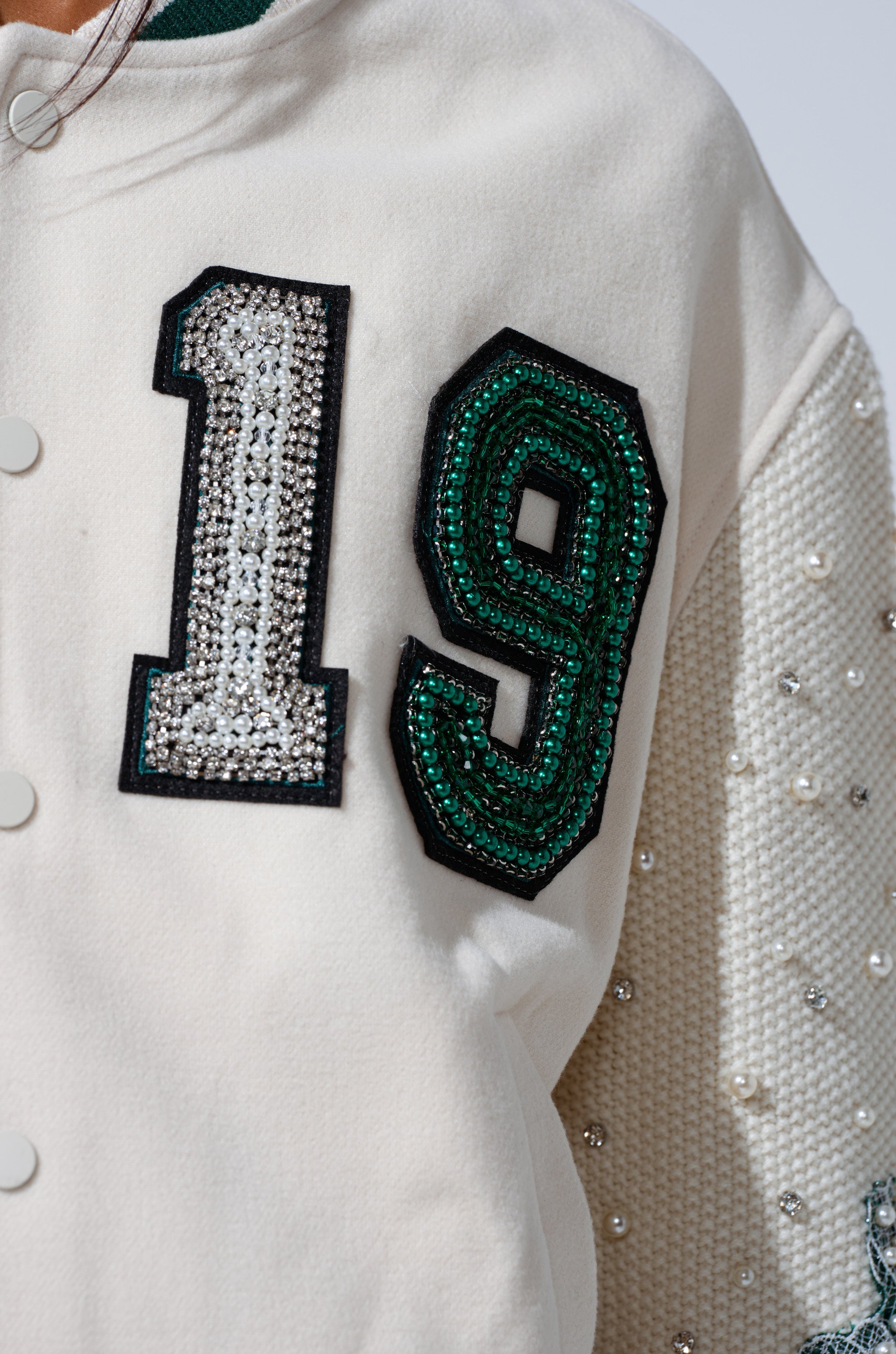A close-up of the BETTER LUCK NEXT TIME EMBELLISHED BOMBER shows '19' in patches—'1' with silver rhinestones, '9' with green and black sequins. The jacket’s sleeve features small pearls.