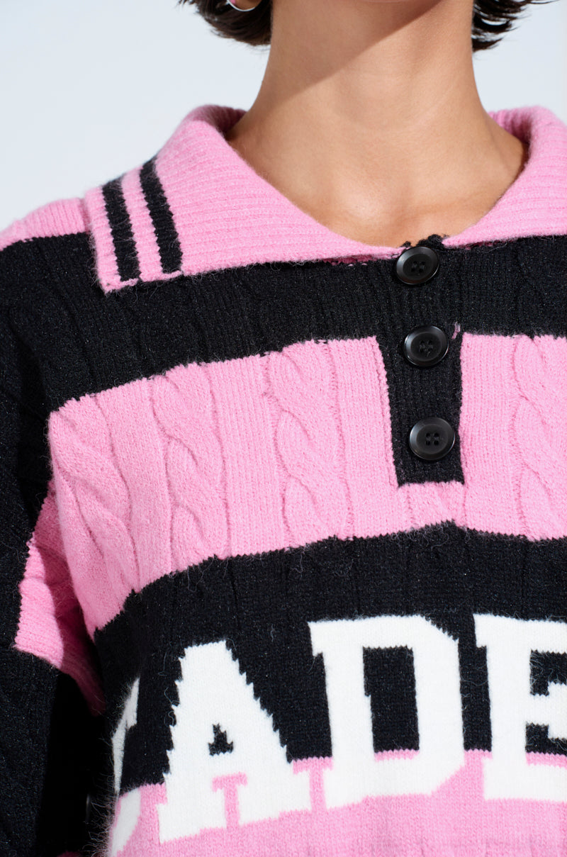 Close-up of a person wearing the ACADEMIC STRIPE SWEATER—an oversized pink and black cable-knit style with thick horizontal stripes, a collar, three black buttons, and bold partial white block letters across the chest.