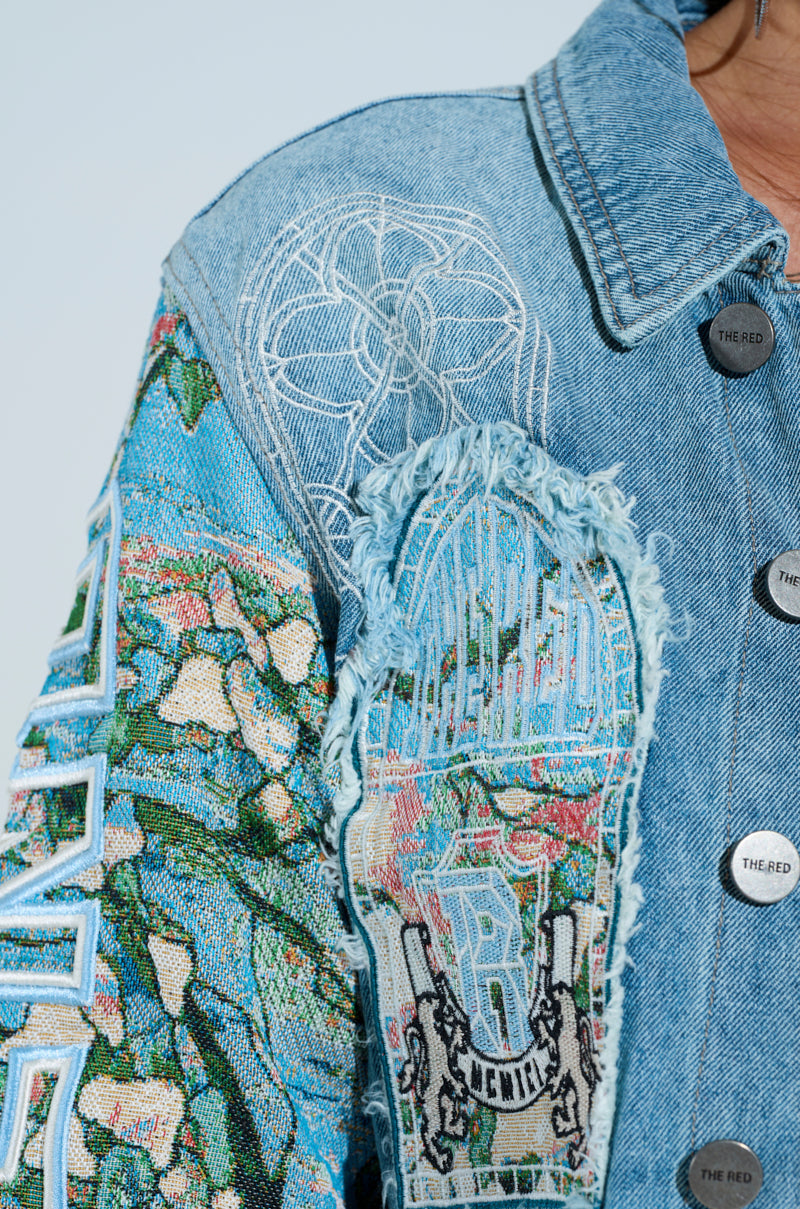 Close-up of the OUT OF THIS WORLD DENIM JACKET in a cropped silhouette with intricate embroidery and graphic patches. It features colorful floral designs on the left shoulder, frayed patches, threaded patterns on the front, and silver buttons engraved with "THEREID" down the front.