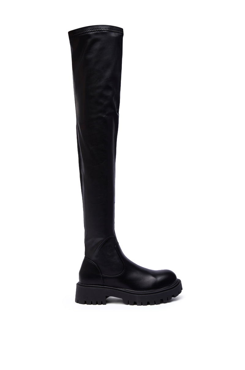 The AZALEA WANG AJUNA Black Flat Thigh High Stretch PU Boot features a black stretch fit, chunky sole, and round toe. Displayed upright on a white background, it’s perfect for fans of stylish over-the-knee boots.