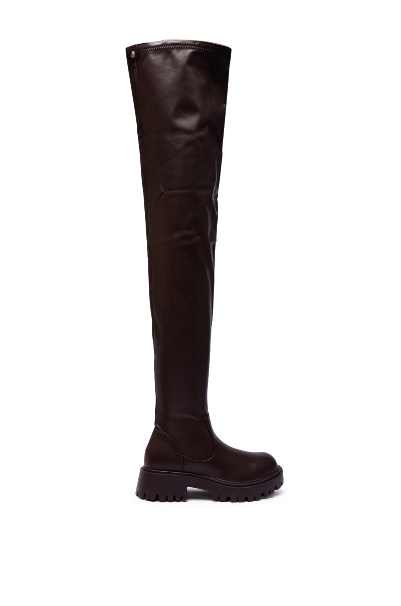 The AZALEA WANG AJUNA Chocolate Four Way Stretch PU Flat Boot is shown in profile—an over-the-knee, dark brown faux leather boot with a round toe, against a white background.