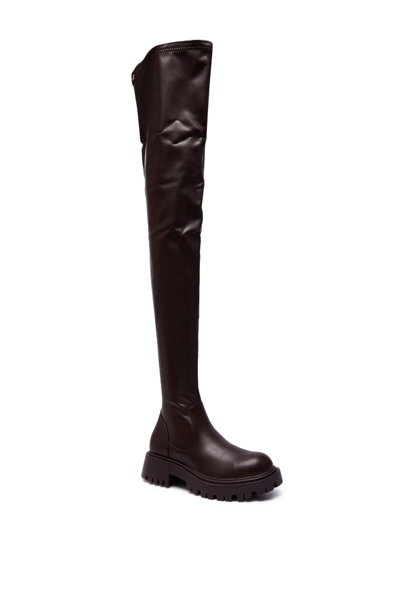 The AZALEA WANG AJUNA Chocolate Four Way Stretch PU Flat Boot is an over-the-knee, dark brown faux leather boot with a chunky treaded sole and round toe, shown against a white background.