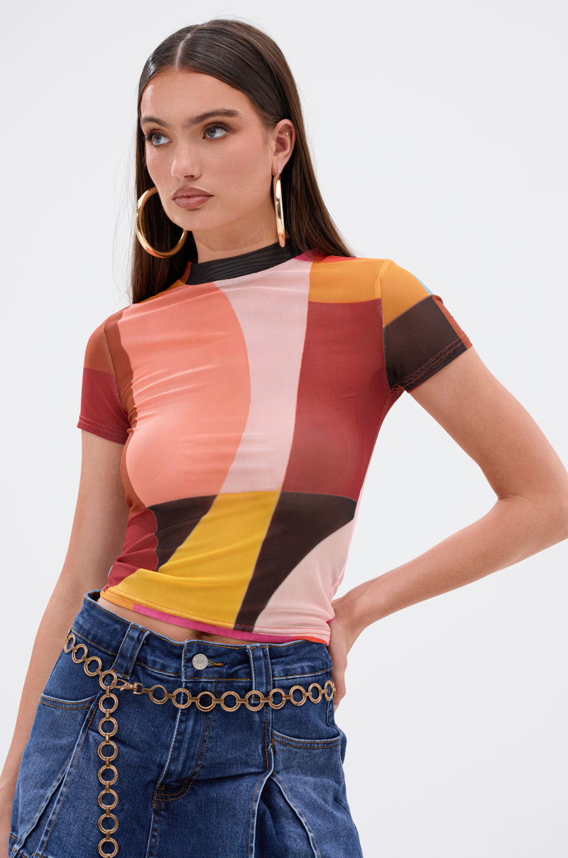 A woman poses against a plain white background wearing large hoop earrings, a chain belt, blue denim jeans, and the ABSTRACT THOUGHTS MESH SHORT SLEEVE TEE featuring an abstract graphic print.