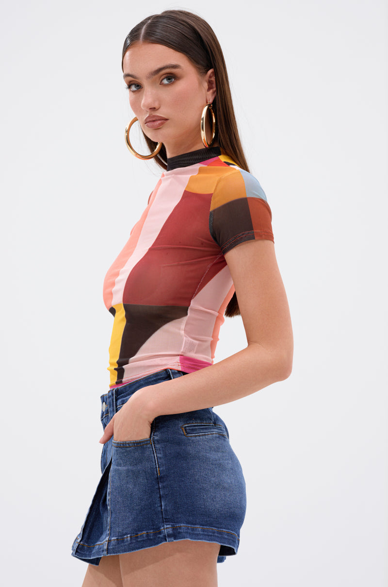 A woman with long brown hair wears large hoop earrings, blue denim shorts, and the ABSTRACT THOUGHTS MESH SHORT SLEEVE TEE. She stands sideways with one hand in her pocket against a plain white background.