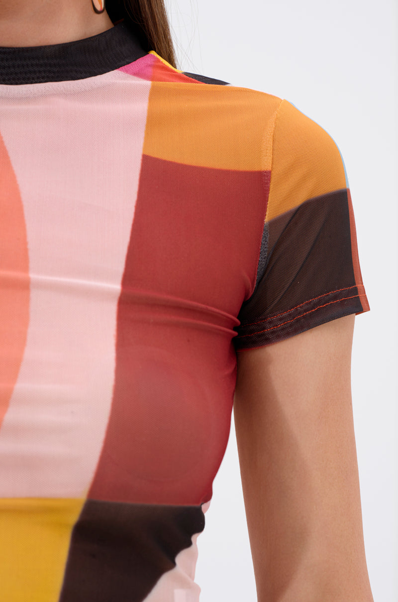 Close-up of a person wearing the ABSTRACT THOUGHTS MESH SHORT SLEEVE TEE, featuring an abstract graphic with colorful geometric blocks in pink, orange, yellow, red, and black. Only the shoulder, arm, and upper chest are visible.