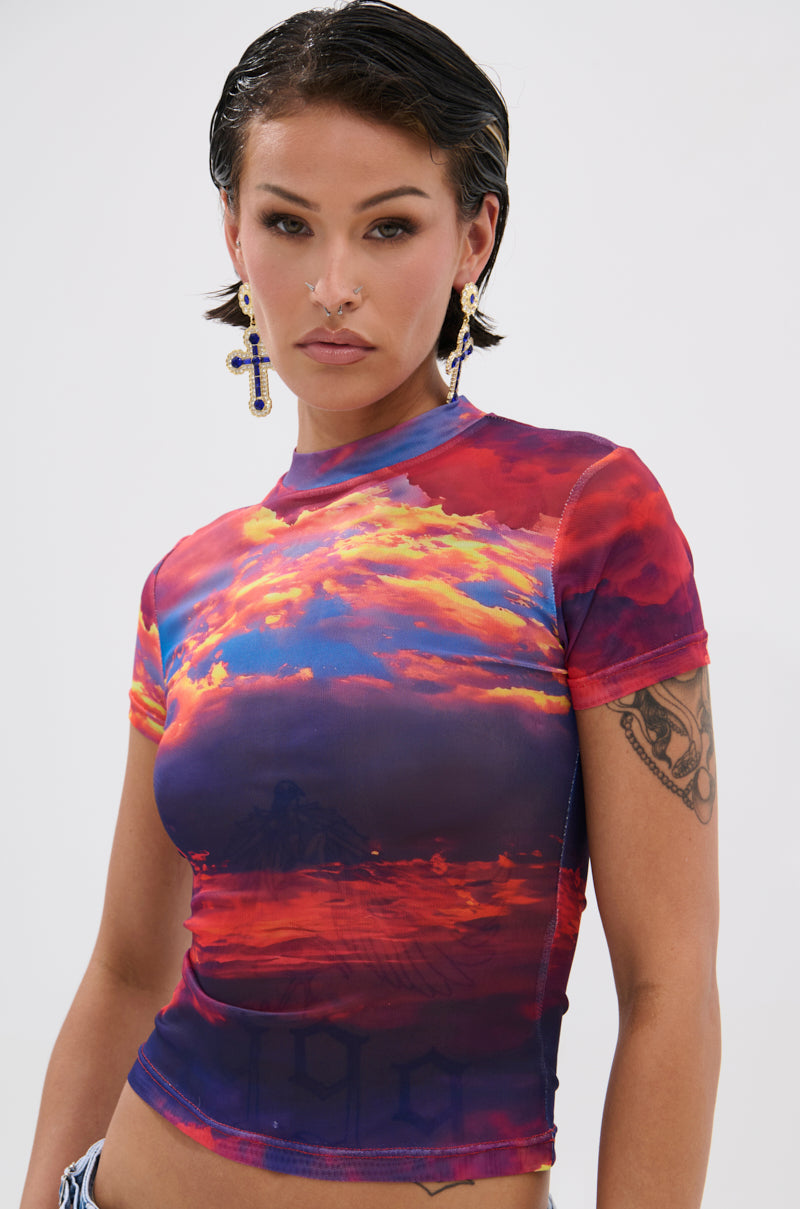 A person with short dark hair, bold makeup, cross earrings, and a visible upper right arm tattoo wears the HEAD IN THE CLOUDS MESH SHORT SLEEVE TEE. The colorful fitted mesh top stands out against the plain white background. 0