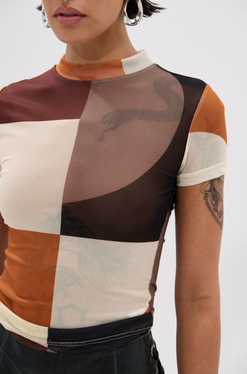 Wearing the SYMBOLISM MESH SHORT SLEEVE TEE featuring bold geometric color blocks in brown, cream, and orange, a person exudes a retro vibe. Silver hoop earrings and an upper arm tattoo complete the look; image cropped at shoulders.