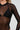 The image captures a person wearing the NEW BODY LONG SLEEVE MESH BODYSUIT in black, styled over a black bra. The photo is cropped to highlight the upper body from shoulders to waist, set against a neutral gray background.