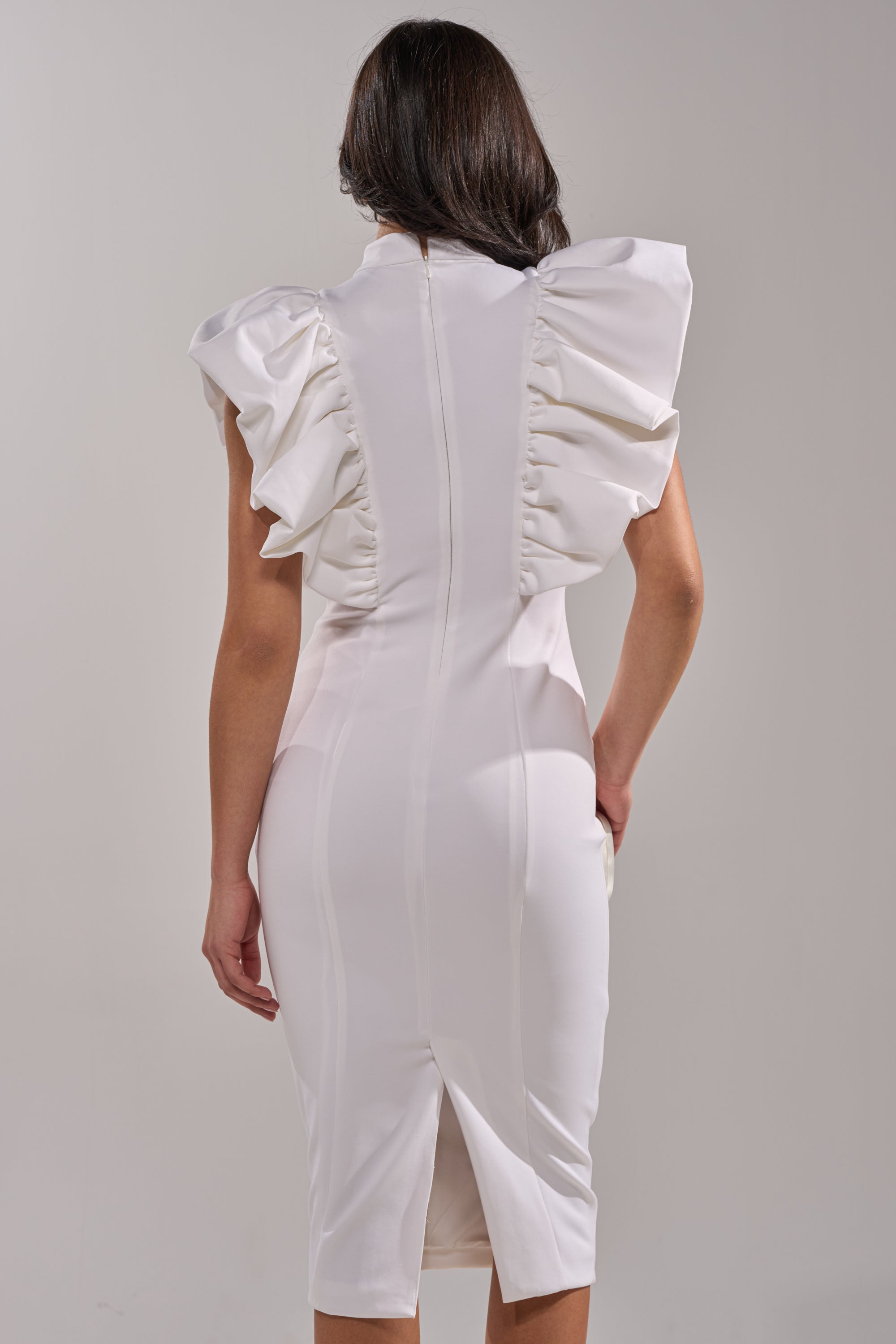 A woman with dark hair down is seen from the back wearing the TRUTH BE TOLD MIDI DRESS IN WHITE, featuring puffed ruffled sleeves, a visible seam, and a back slit against a plain light background. 3
