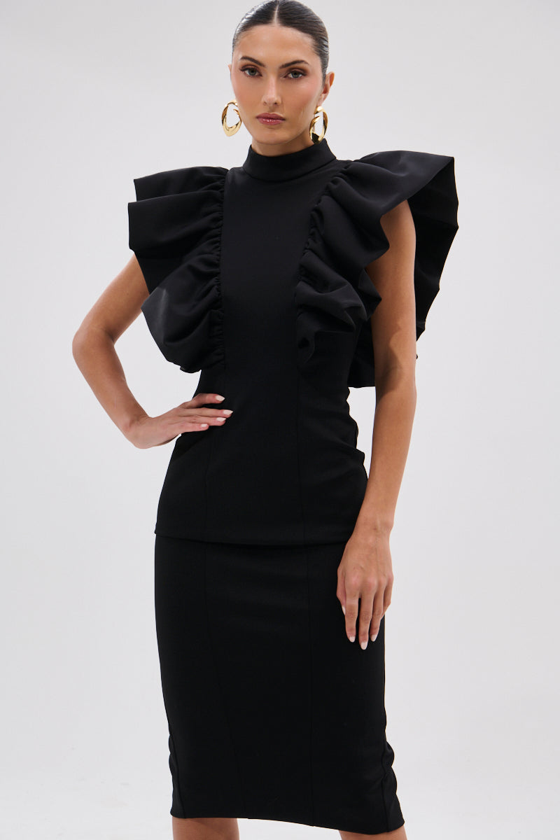 A woman poses against a plain white backdrop wearing the TRUTH BE TOLD MIDI DRESS, featuring a fitted black silhouette with sculptural ruffle shoulders, gold hoop earrings, and slicked-back hair. 6