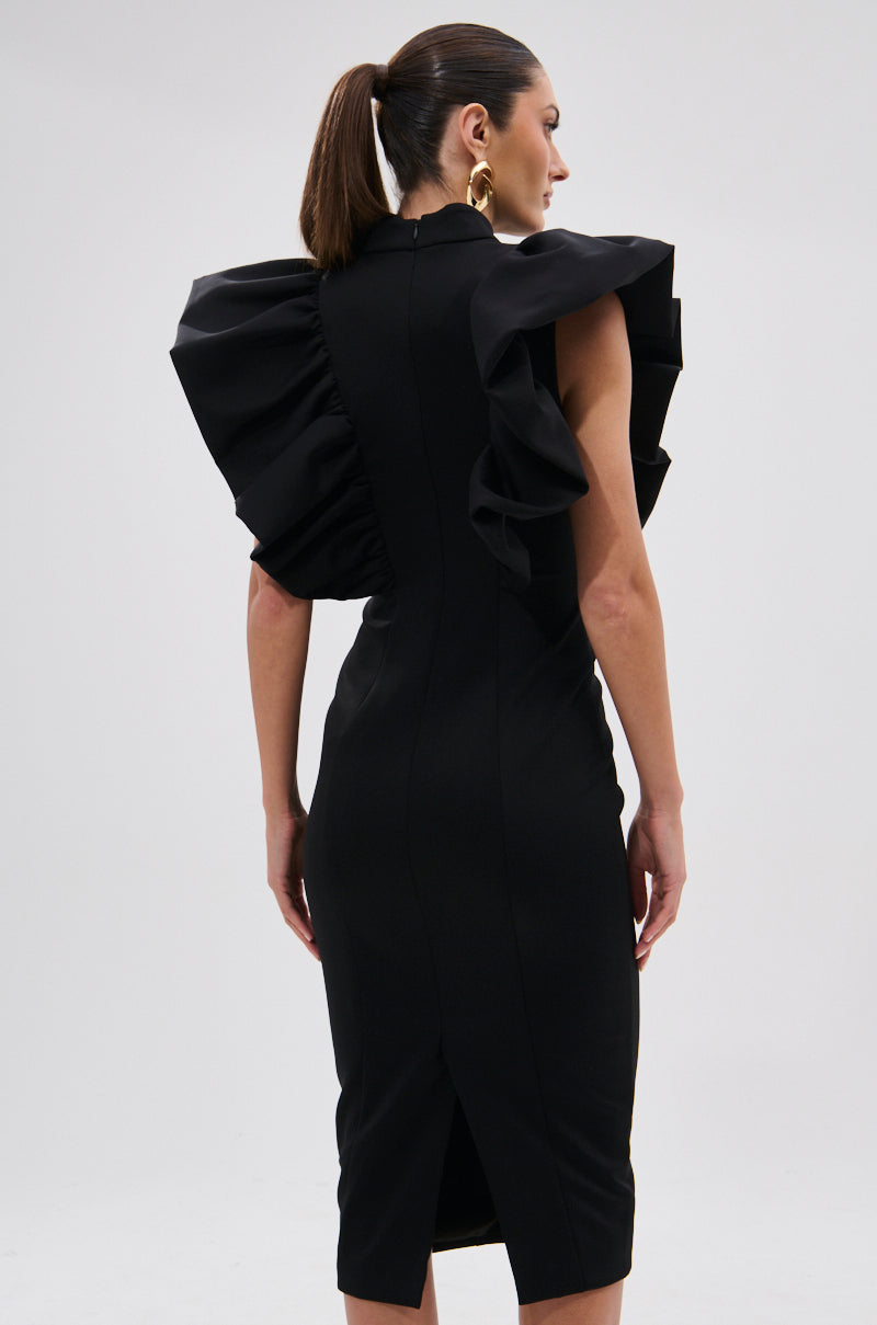 A woman faces away, wearing the TRUTH BE TOLD MIDI DRESS, a fitted black dress with sculptural ruffle shoulders. Her hair is styled in a sleek ponytail and she wears large gold hoop earrings against a plain light background. 11