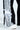 A close-up showcases the DYLAN LACE DETAIL WIDE LEG DENIM in black with vertical black and white stripes, ornate lace trim, and a tied white ribbon on one leg. The high-rise fit complements white sneakers as the wearer stands on a light surface.