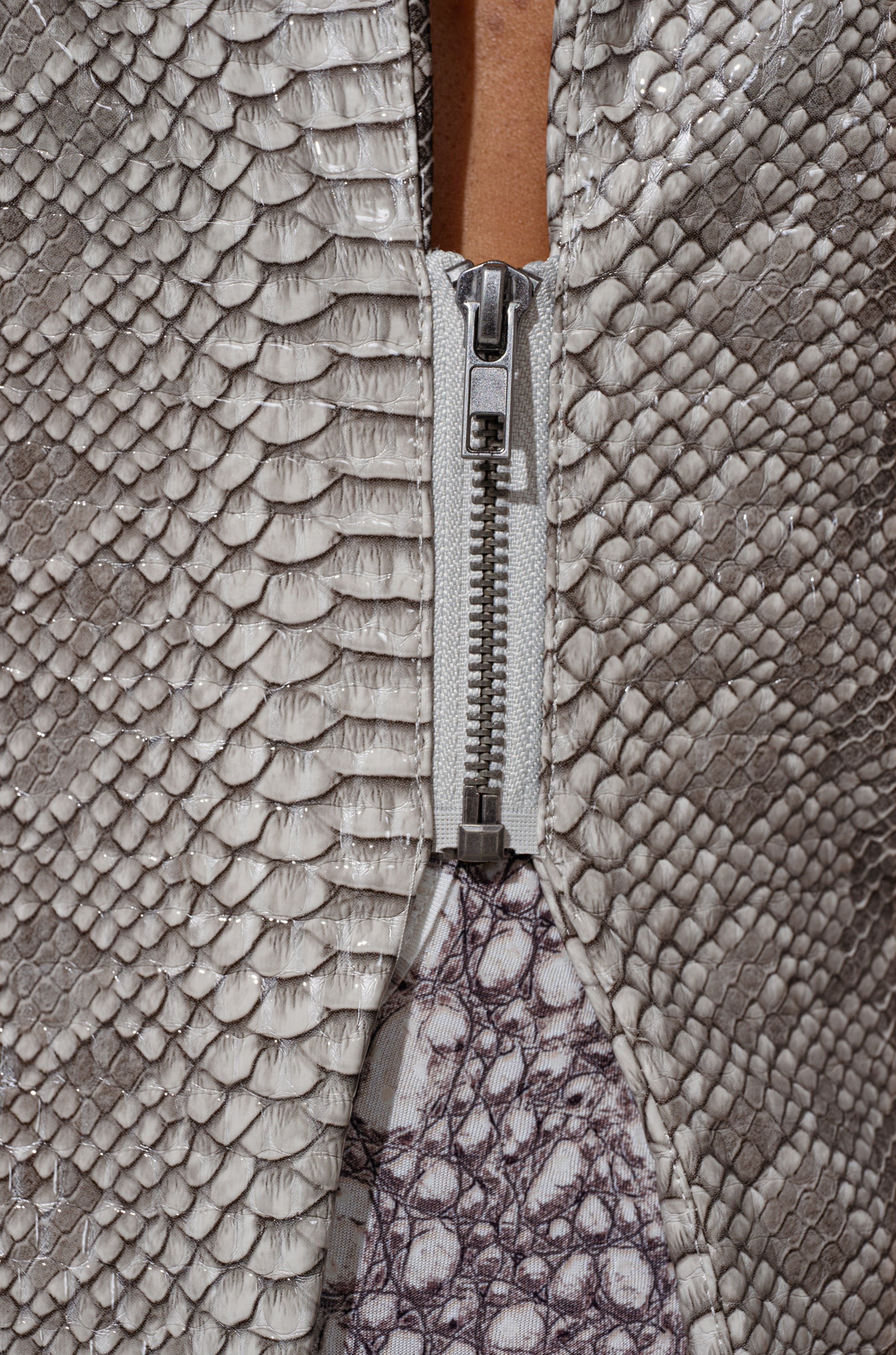 Close-up of the silver zipper on the LILA CUTOUT TRENCH, featuring textured light gray faux snakeskin and a peek of white and gray patterned lining. 6