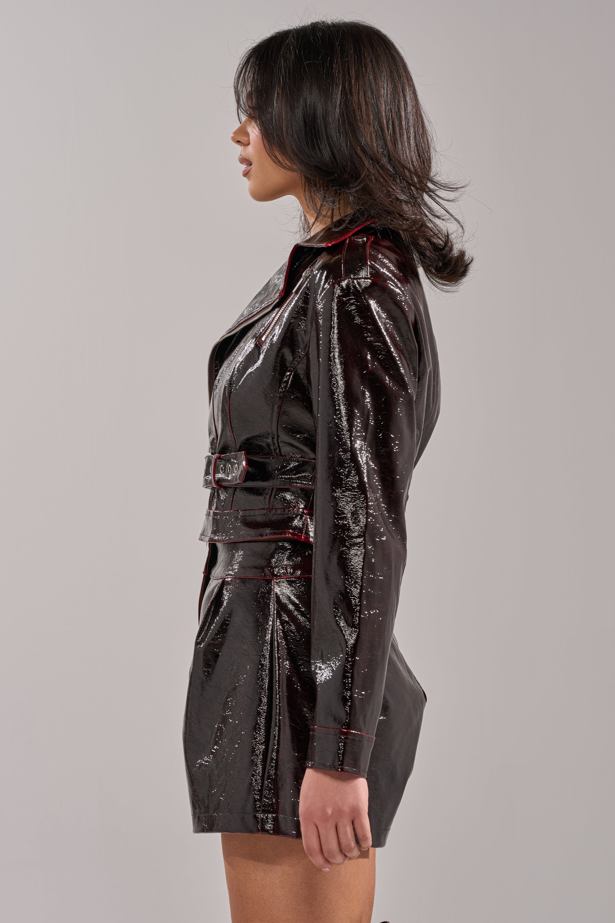 A person with shoulder-length dark hair stands in profile, wearing THE WAY YOU MOVE COLOR CHANGING MOTO jacket and matching skirt against a plain light gray background. 3