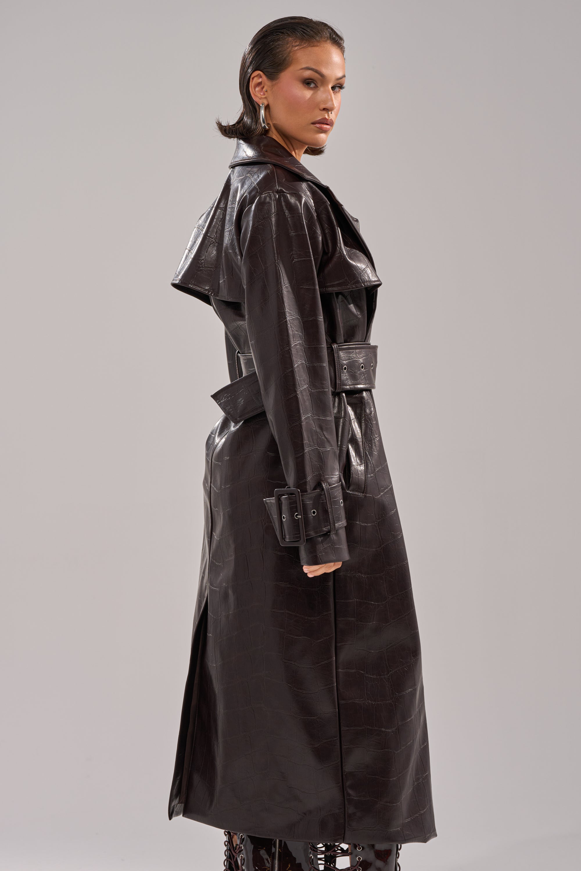 A woman with slicked-back hair poses in the EMBOSSED CROC TRENCH, looking over her shoulder against a plain light gray background. 2