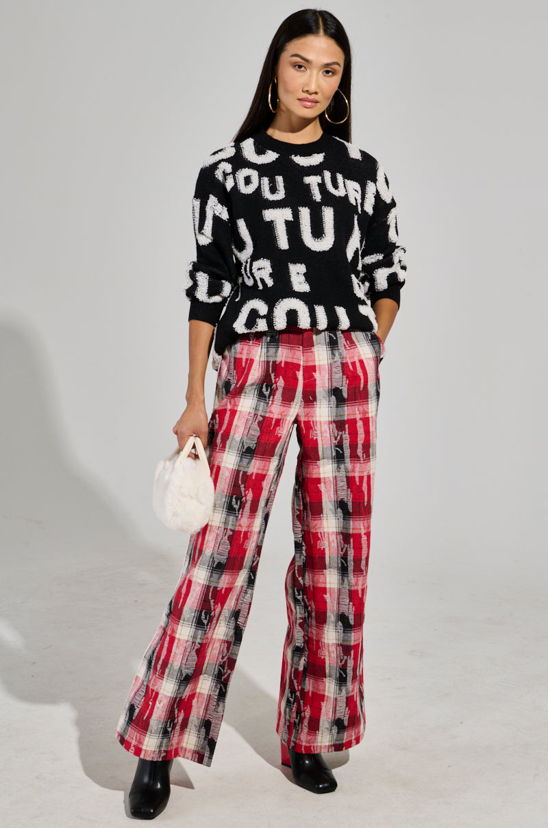 A woman wearing the FOREVER COUTURE LONG SLEEVE KNIT SWEATER, paired with red plaid wide-legged pants, stands confidently. She holds a small white fuzzy bag and wears black boots. Her long hair is down, and she accessorizes with large hoop earrings. 5