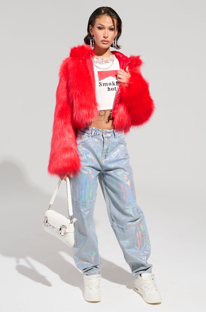 A model poses against a white backdrop, showcasing the MAEVE Hooded Red Faux Fur Bomber over a cropped T-shirt with text, complete with holographic pants and white sneakers. She carries a white shoulder bag and enhances her look with hoop earrings and chunky necklaces.