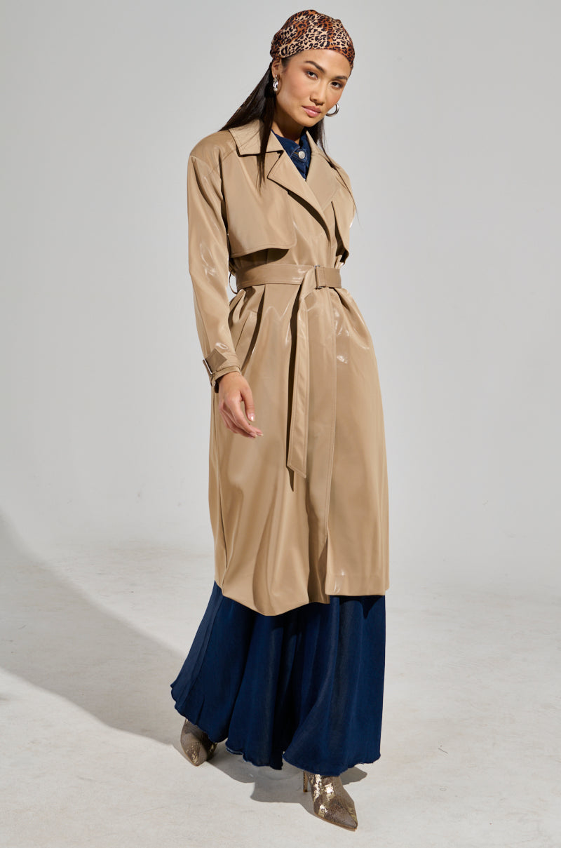 Wearing the LEAH LO LIQUID VELVET TRENCH over a navy blue dress with metallic ankle boots, the person strikes a pose against a neutral background. A patterned scarf adorns their head, and they finish the look with dangle earrings, embodying style and confidence.