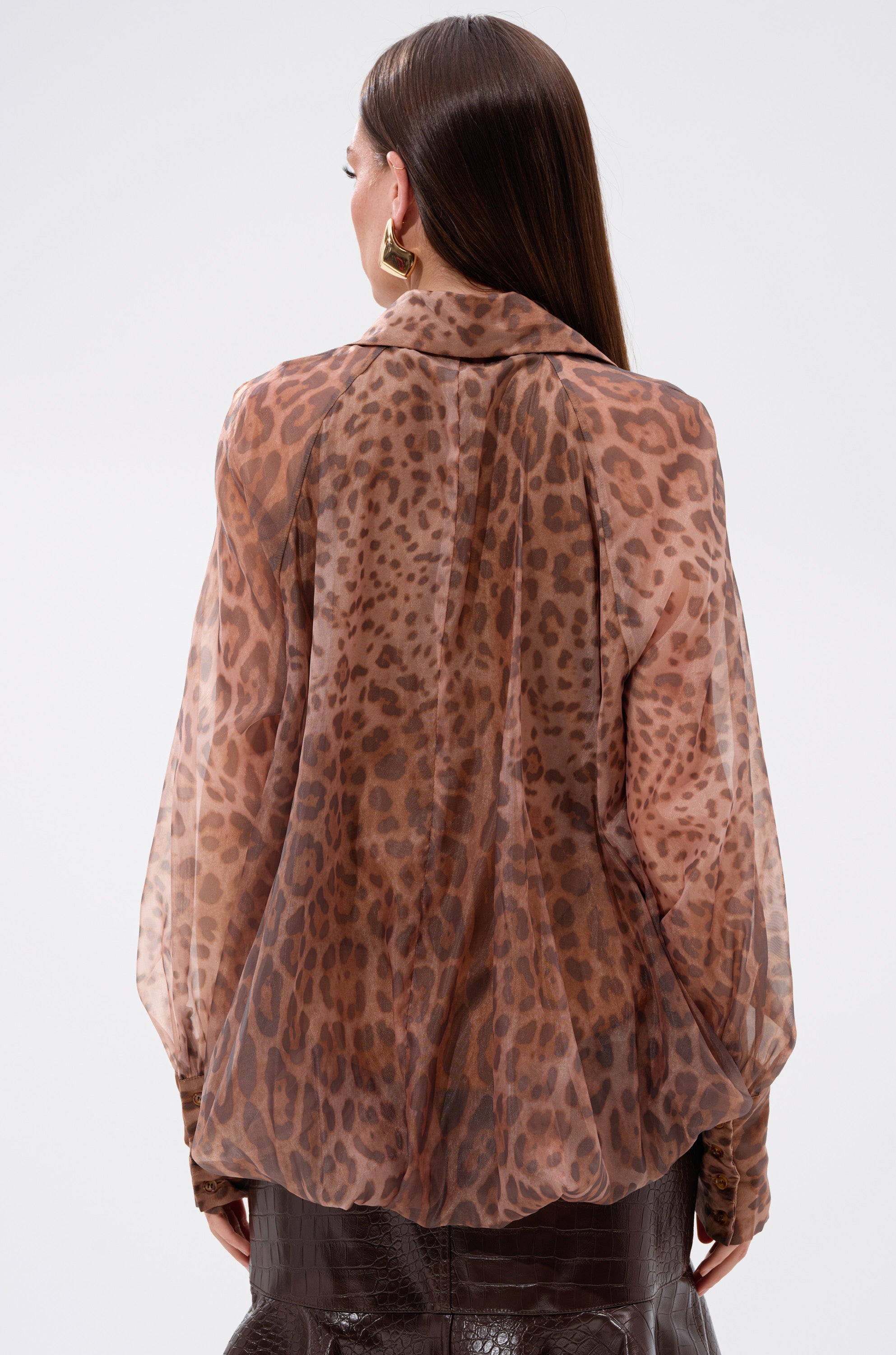 A woman with straight brown hair, gold hoop earrings, and wearing the WILD SPIRIT HIGH LOW SHEER BLOUSE is shown from the back against a plain white background.
