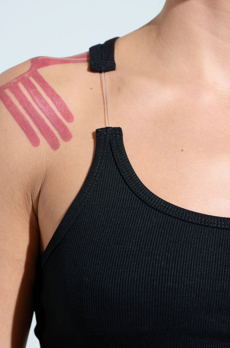 Close-up of a person wearing the BAD HABIT STRAPPY TANK TOP IN BLACK, showcasing a tattoo of pink lines on their shoulder against a plain light background.