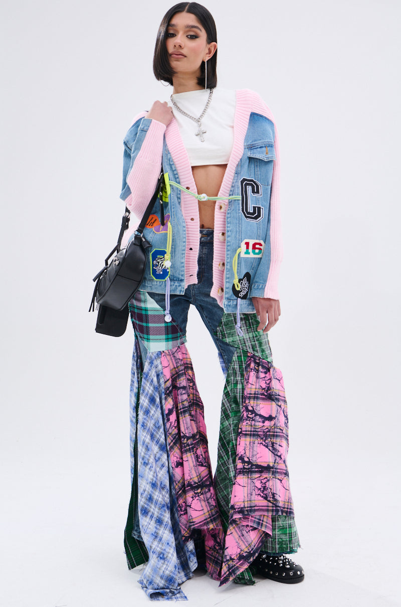 A woman models a cropped white top, the oversized SURGICAL SPLICED CARDIGAN in knit, flared patchwork plaid pants, black studded shoes, and a black shoulder bag against a plain white background. 10