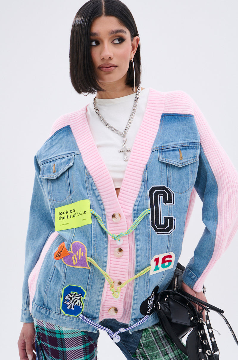A woman wears the SURGICAL SPLICED CARDIGAN—a denim and pink knit jacket with colorful patches—over a white top, styled with checkered pants, hoop earrings, layered necklaces, and straight dark hair. 4