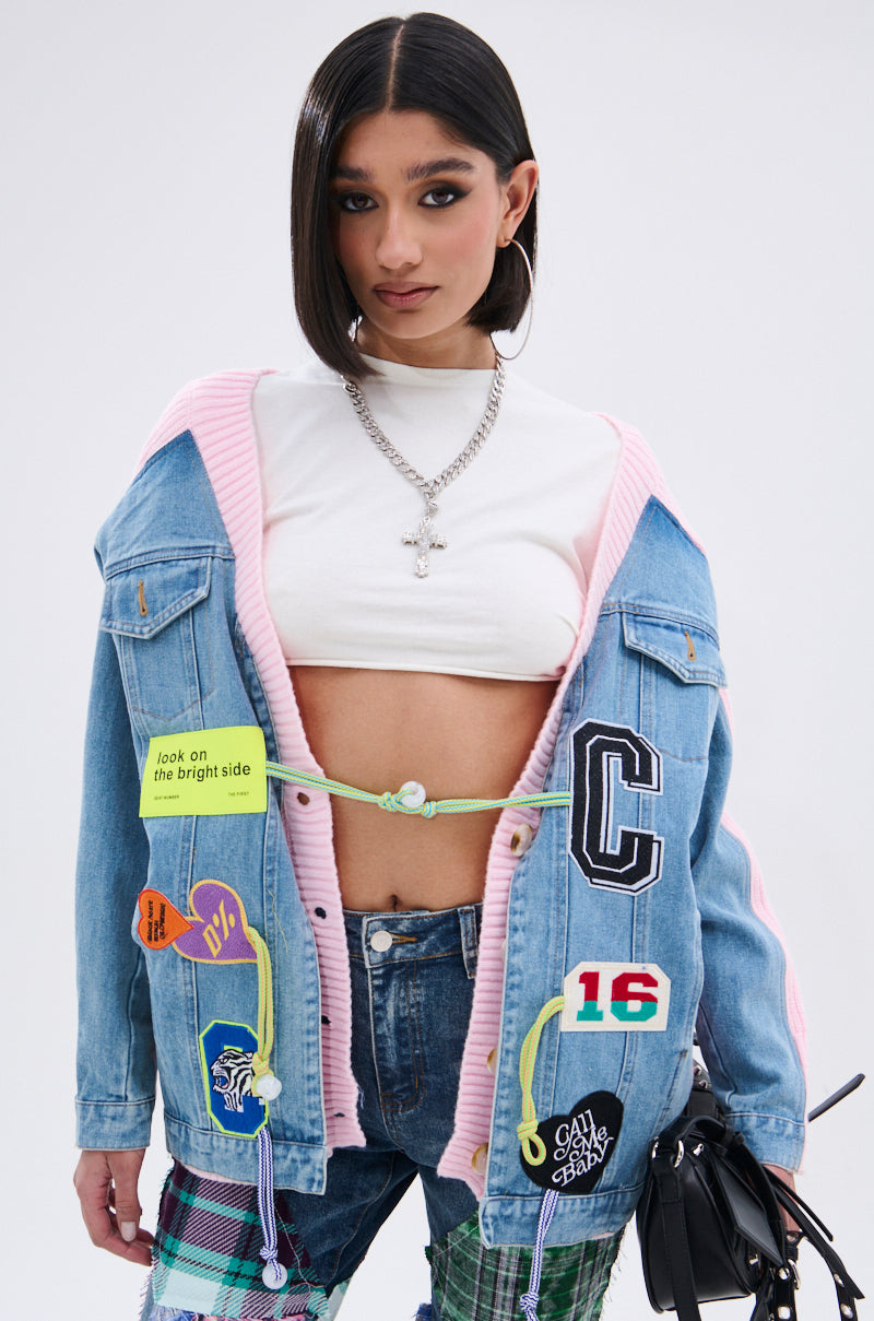 A woman with straight dark hair wears a white crop top, silver chains, and an oversized patchwork denim jacket, plaid pants, and a black bag. Her style is completed with the SURGICAL SPLICED CARDIGAN in soft knit fabrication. 5