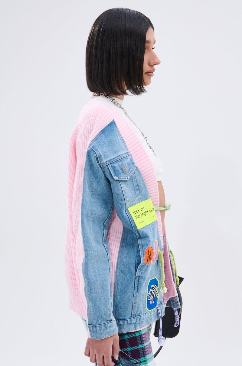 A woman with straight black hair, wearing a denim jacket decorated with colorful patches and the SURGICAL SPLICED CARDIGAN draped over her shoulders, stands in profile against a plain white background. 6