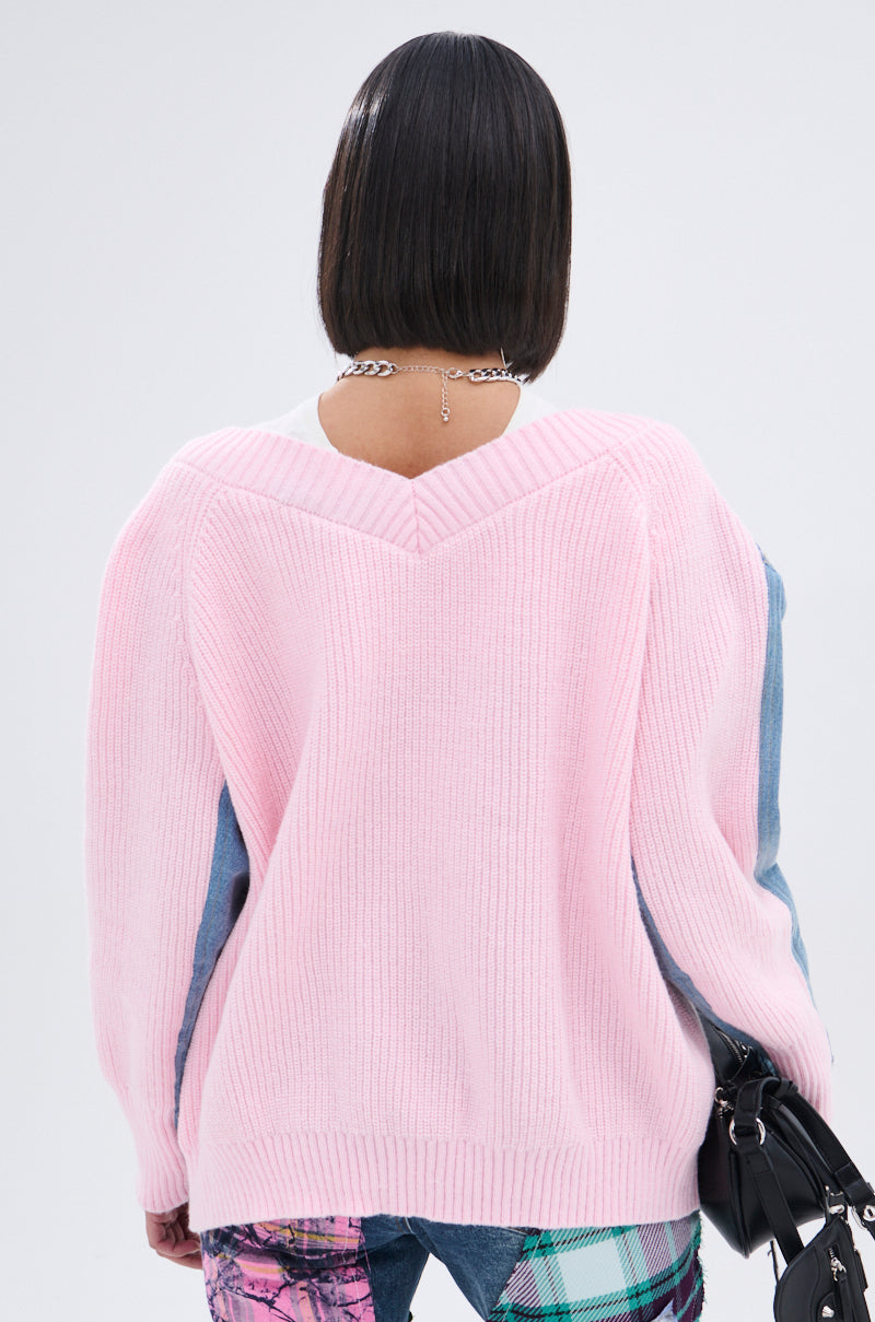 A person with a short bob haircut is seen from behind, wearing the SURGICAL SPLICED CARDIGAN in light pink and blue knit, patterned jeans, a silver chain necklace, and holding a black handbag. 8