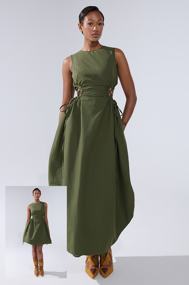 A woman models the ALINA LACE UP DETAIL MAXI DRESS IN OLIVE, featuring side ties, against a light gray backdrop. An inset shows a full-length view, displaying her complete outfit including mustard lace-up shoes.