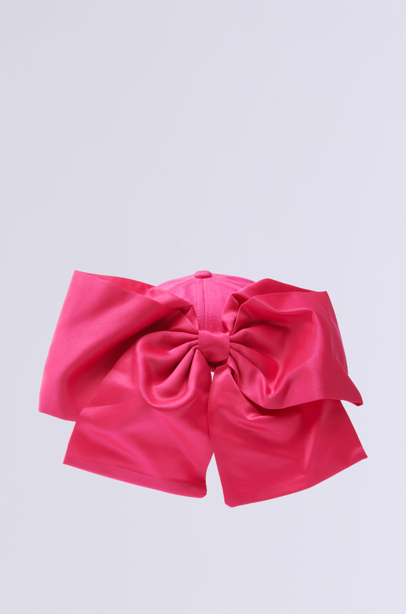 A chic VALENTINA BOW HAT features a large, vibrant pink satin bow with a gathered center and wide, flowing loops and tails against a light gray background.
