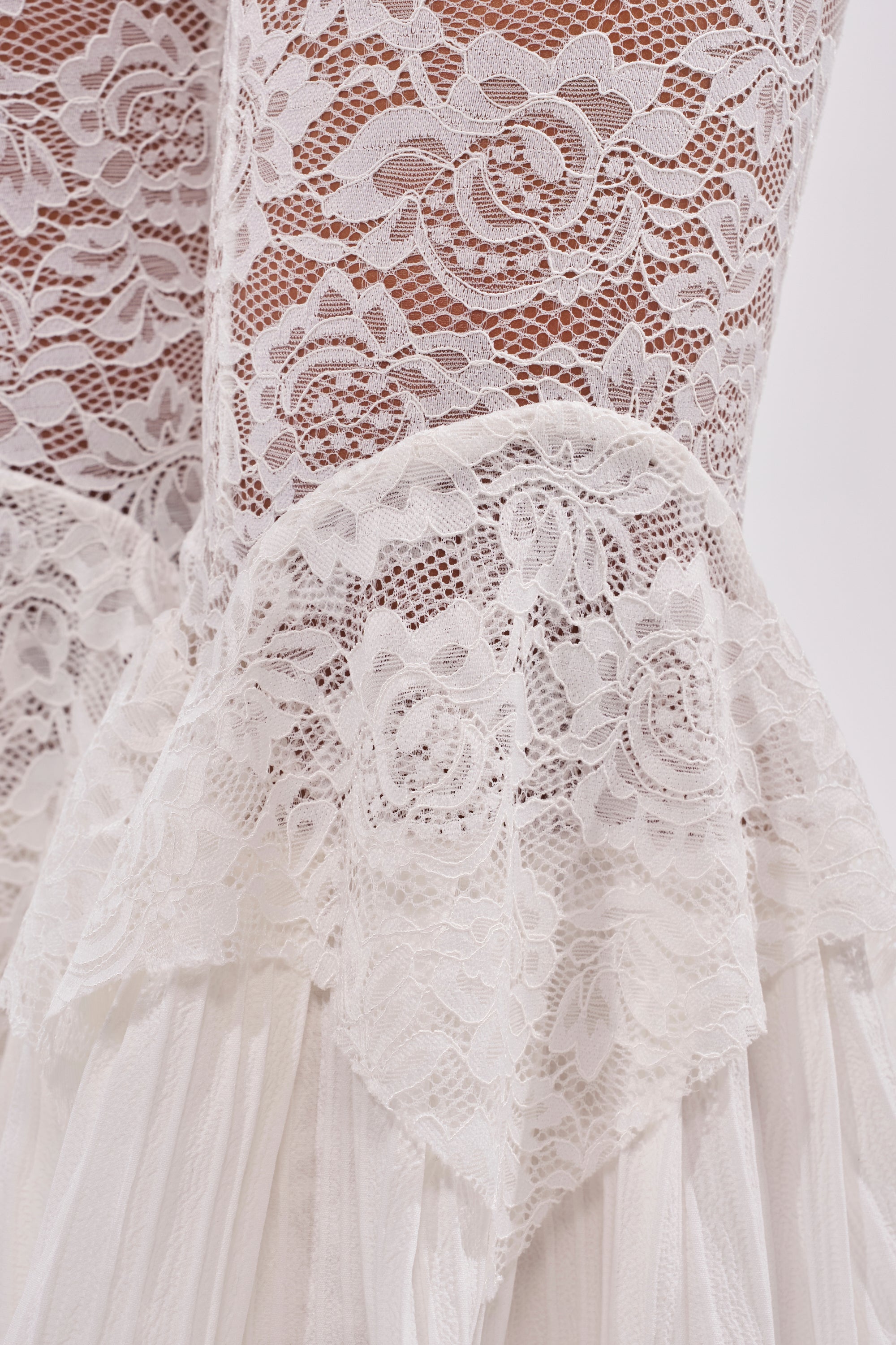 Close-up of white floral lace with rose designs and scalloped edges layered over sheer fabric—COACHELLA LACE RUFFLE PANTS are perfect for elevating your festival style with boho-chic flair. 9