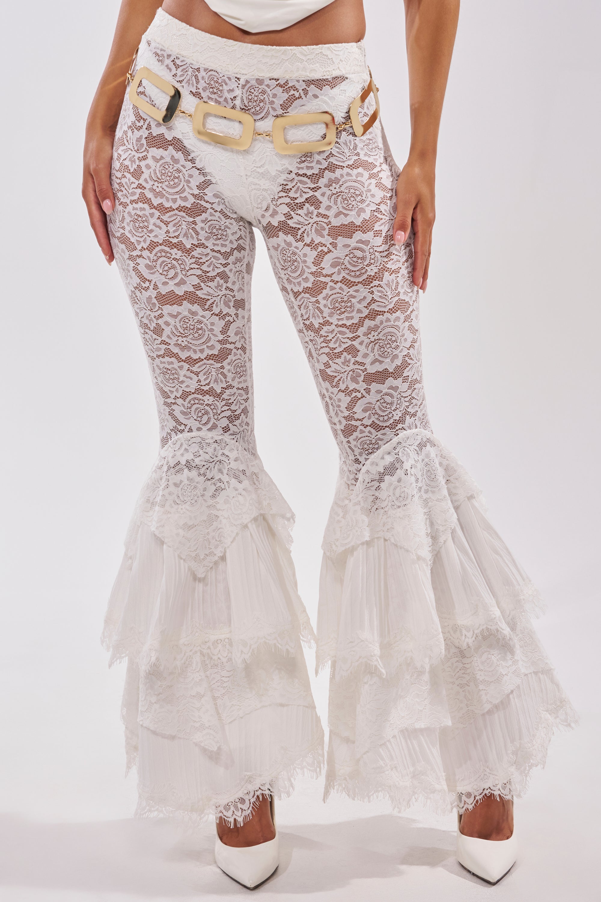 Someone styled the COACHELLA LACE RUFFLE PANTS—white, sheer lace with ruffled hems and a wide belt featuring bold rectangular links—with white high heels for a chic boho look. 0