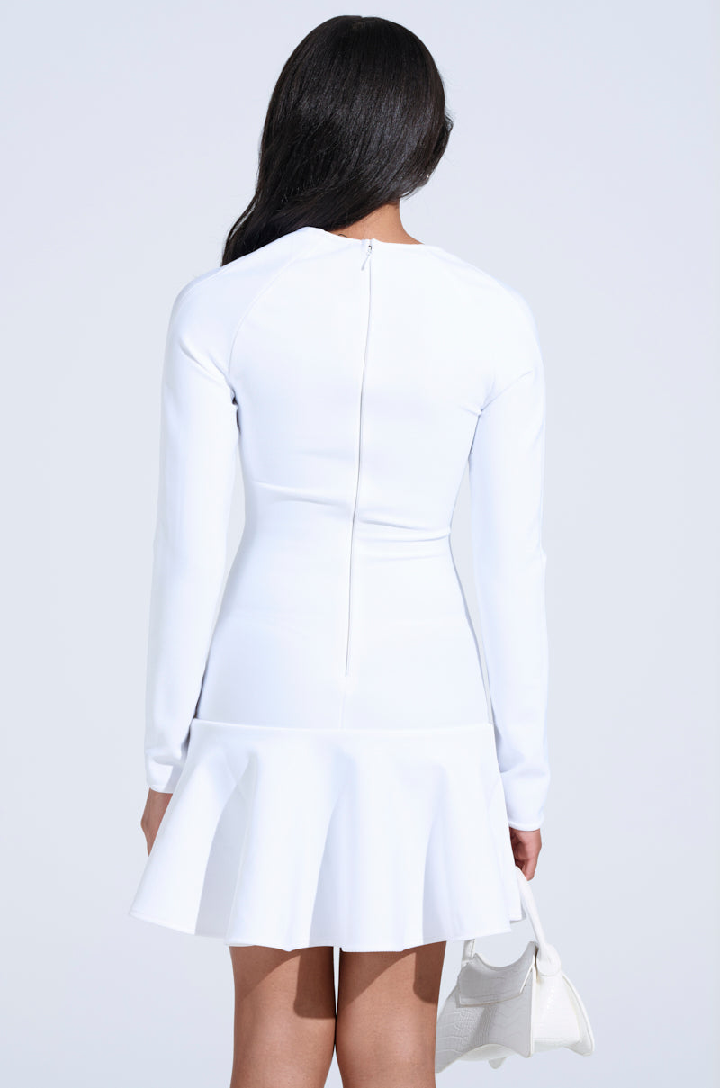 A person with long dark hair is seen from behind wearing the Highly Favored Bandage Mini Dress in White, featuring a flared skirt and sweetheart neckline. They hold a small white handbag against the light gray background.