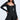 A woman stands confidently against a plain background, wearing the IN THE MOOD BANDAGE MINI DRESS—a fitted, off-shoulder black mini with long sleeves, a sweetheart neckline, and a flared skirt—looking elegantly to the side.