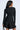 A woman with long dark hair is seen from the back wearing the IN THE MOOD BANDAGE MINI DRESS, a fitted mini with long sleeves and a flared skirt, holding a small bag in her left hand against a plain white background.