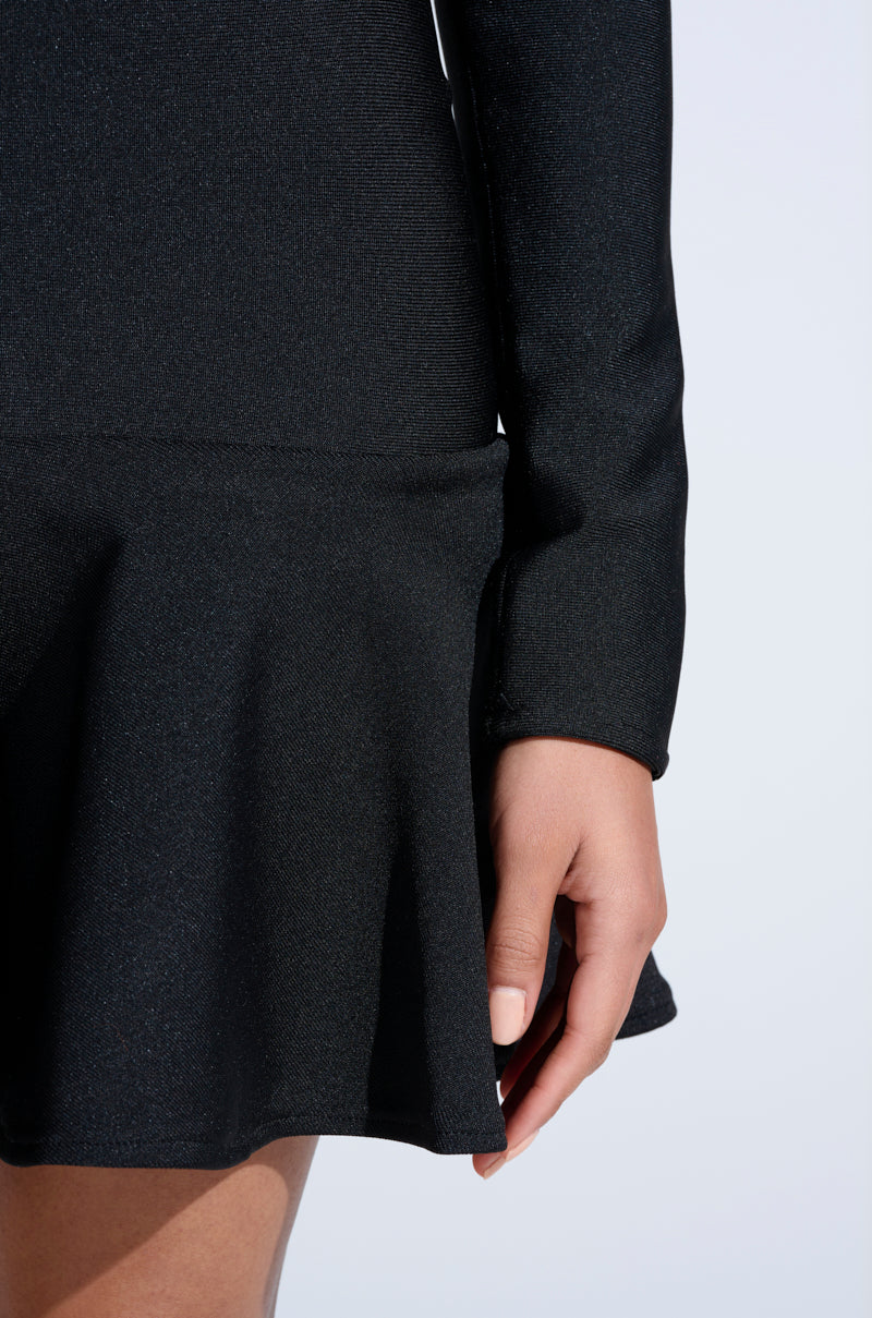 A close-up of a person wearing the IN THE MOOD BANDAGE MINI DRESS, showing only the lower part of the flared skirt and their right hand against a light background.