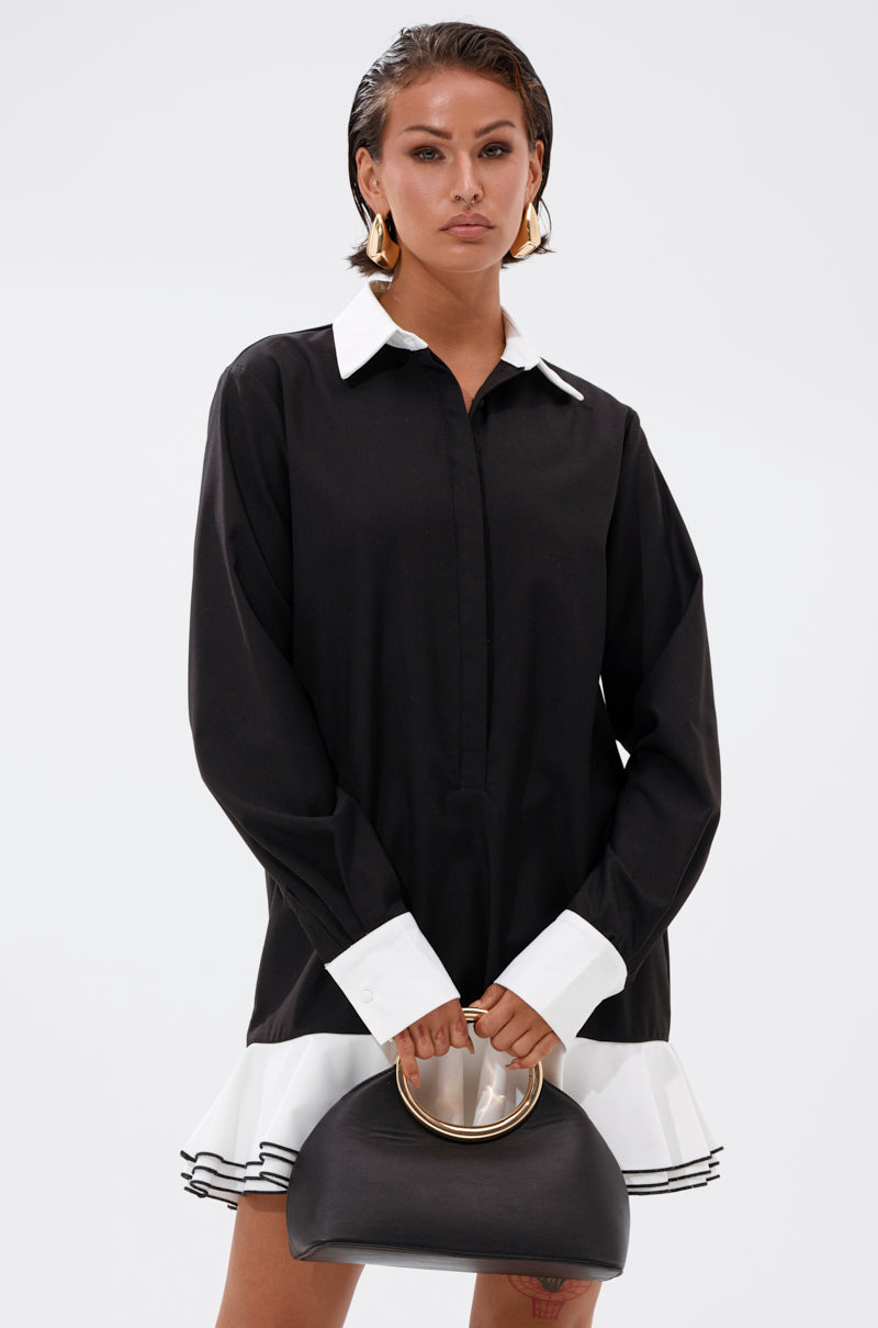 Woman wearing the ALWAYS CLASSY POPLIN SHIRT DRESS, a long-sleeved black shirt dress with white cuffs and collar, holding a black handbag with a gold handle against a plain white background.