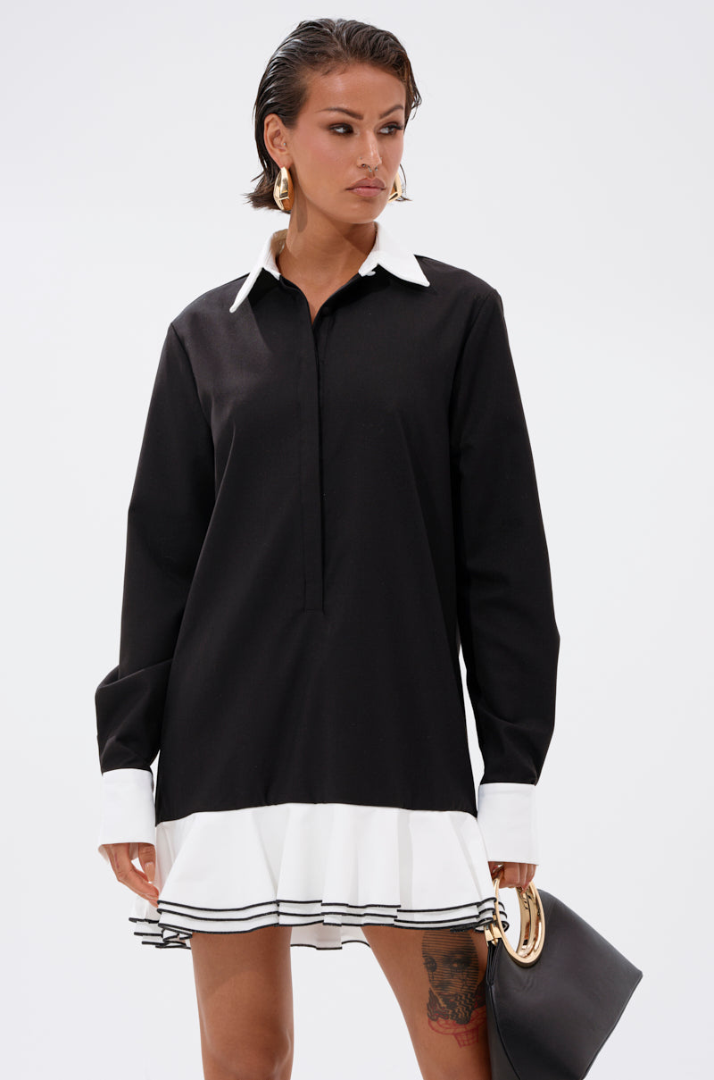 A woman wears the ALWAYS CLASSY POPLIN SHIRT DRESS with a white collar, white cuffs, and ruffled hem. She accessorizes with a black clutch, gold hoop earrings, short wet-look hair, and displays her leg tattoo.
