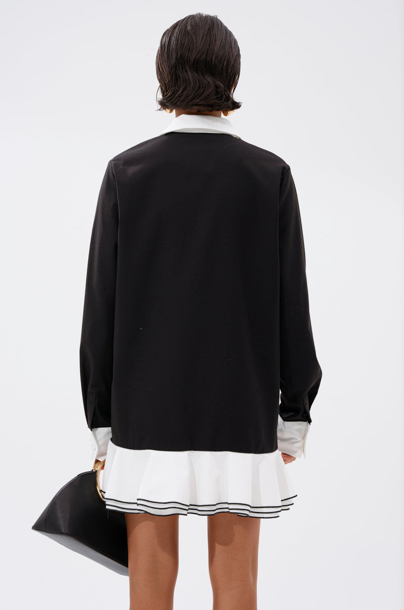 A person with short dark hair is shown from the back, wearing the ALWAYS CLASSY POPLIN SHIRT DRESS featuring a white collar and white ruffled hem, holding a black bag against a plain white background.