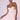 A model with a sleek hairstyle poses in the FELT CUTE SATIN MINI DRESS, showcasing its light pink, satin fabric and thin spaghetti straps. The mini dress boasts a ruched, corset-inspired bodice and a ballet-style skirt. She enhances her look with gold hoop earrings and a delicate gold necklace.