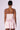 The image shows the back view of a person wearing the FELT CUTE SATIN MINI DRESS, featuring a pink satin mini dress with a corset-inspired bodice that flares out into a ballet-style skirt. The person has short hair styled in a slicked-back manner and is also wearing hoop earrings.