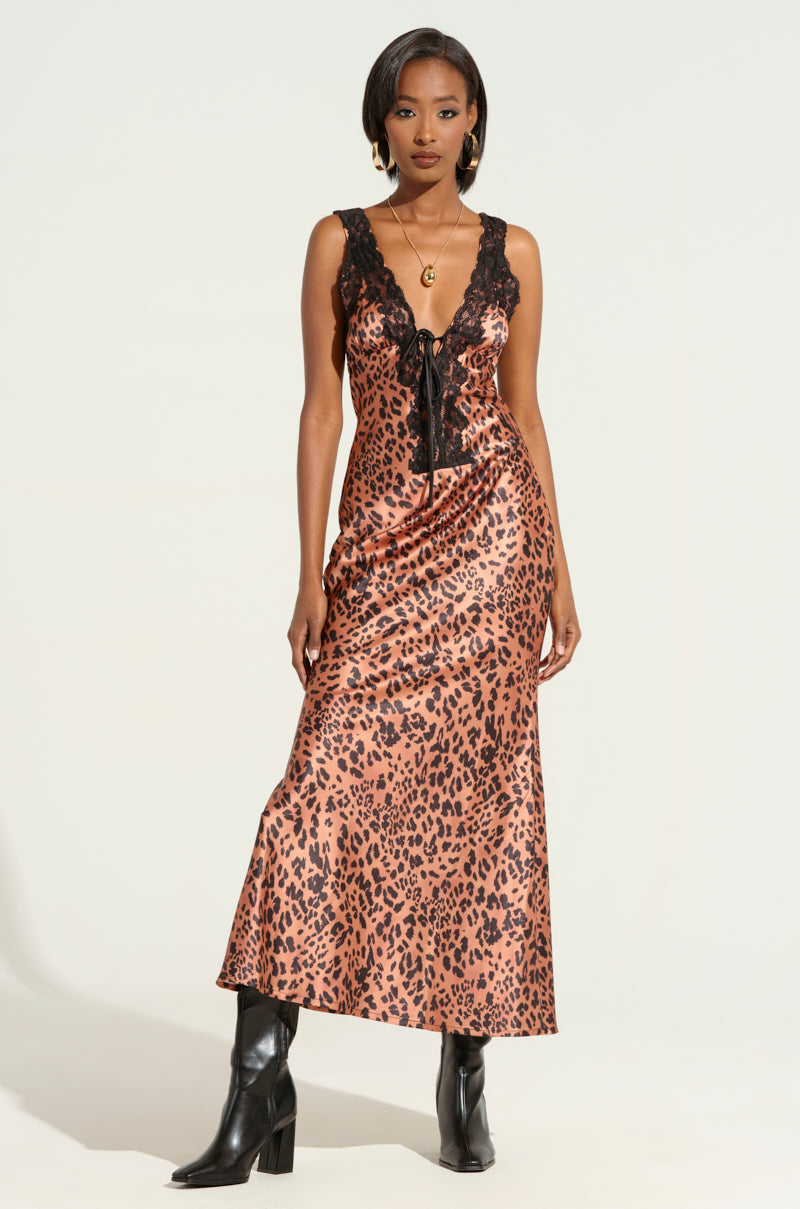 Wearing a chic LEOPARD PRINT IS THE NEW BLACK SATIN MIDI DRESS with lace trim, the individual exudes confidence in black boots and a pendant necklace.