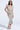 A woman models the I DO WHAT I WANT METALLIC MIDI DRESS IN BEIGE, featuring a plunging V-neckline and ruched detailing, styled with silver heels and a bracelet against a plain light backdrop.