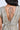A close-up of a person in the I DO WHAT I WANT METALLIC MIDI DRESS IN BEIGE, highlighting the ruched details, deep V-back with thin upper back tie, shimmering fabric, and dark wavy hair cascading to one side.
