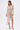 A woman wears the FELT CUTE RUCHED MINI DRESS, a shimmery metallic stretch-knit piece with a deep V-neckline and asymmetrical draped sash, styled with a gold clutch and metallic high-heeled sandals.