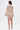 A woman with straight brown hair wears the FELT CUTE RUCHED MINI DRESS in shimmery beige, featuring long sleeves, a deep V-neckline, and side drape detail. She accessorizes with a gold clutch and strappy high-heeled sandals against a white background.