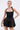 A woman models the LIKE DAYLIGHT SATIN MINI DRESS IN BLACK, featuring halter straps and a flared skirt, paired with hoop earrings and a silver clutch against a plain background.